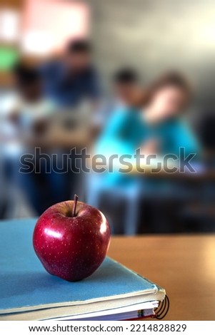 Apple on teacher table in classroom. Blurred background scene of student doing homework. Focus on foreground. Vertical.