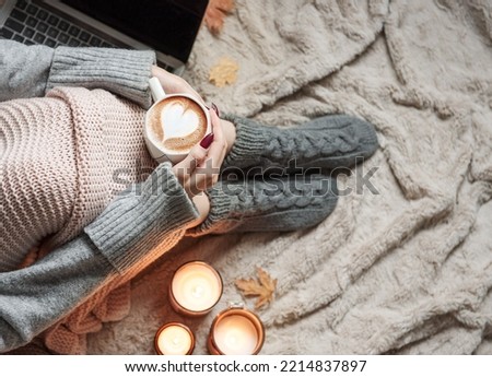 Cozy home, woman covered with warm blanket, drinks coffee and works on a laptop. Relax, carefree, comfort lifestyle.