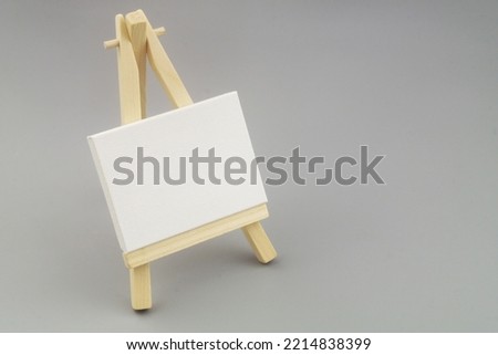 Blank canvas on wooden easel on gray background with space for text.