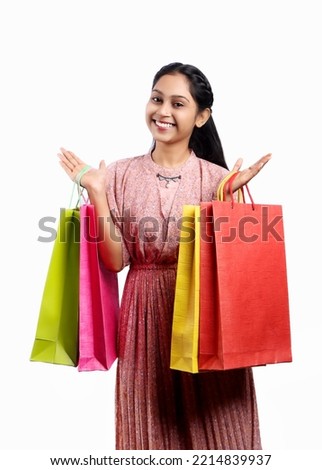 Indian girl holding colourful shoping bags looking towards camera with smile and surprise isolated on white background  Royalty-Free Stock Photo #2214839937