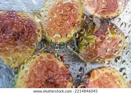 Fresh figs and fig halves on a plate under a film with drops of water. Dark background, close-up view from above.