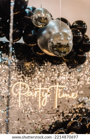 Disco ball. Happy New Year 2023. Bright glowing disco ball on photo booth with decor text party time. Light blur background for wedding or birthday. Zone, wall decorated black and silver balloons.