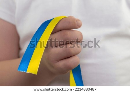 A girl in a white T-shirt holds a yellow-blue ribbon in her hands. State flag of Ukraine. National symbol of Ukraine. Patriot. Close-up