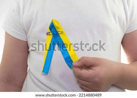 A girl in a white T-shirt with a loop of yellow-blue textile ribbon hanging on it. State flag of Ukraine. National symbol of Ukraine. Patriot. Close-up