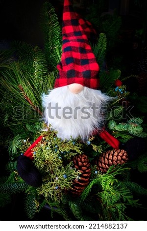 Toy Santa in a checkered hat among coniferous branches and cones on a dark background. Christmas and New Year background.