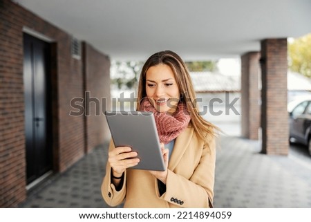 A businesswoman with a tablet outdoors. A happy businesswoman in warm clothes standing outdoors and using the tablet for web research.