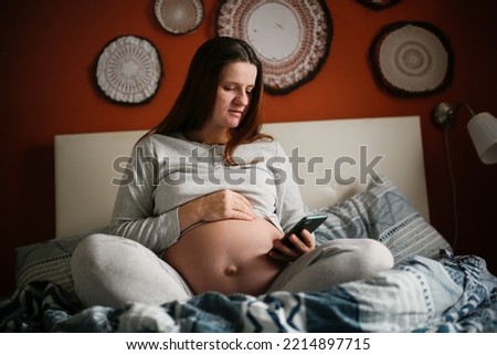 Pregnant woman searching with smartphone in cozy bedroom at home.