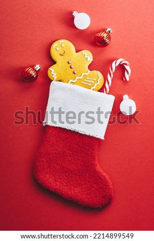 Christmas stocking with gingerbread man cookie, striped candy cane, baubles on red background. Christmas and New Year holiday celebration concept.