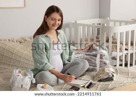 Pregnant woman preparing list of necessary items to bring into maternity hospital in bedroom Royalty-Free Stock Photo #2214911761