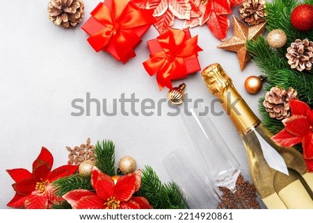 Christmas festive background with champagne bottle and wine glasses, red gift boxes, golden christmas balls, fir branches, poinsettias and decor, top view banner with copy space
