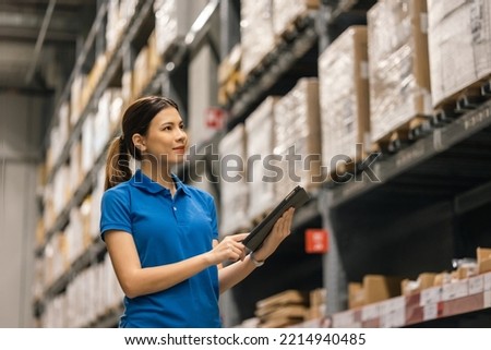 Young female worker in blue uniform checklist manage parcel box product in warehouse. Asian woman employee holding tablet working at store industry. Logistic import export concept. Royalty-Free Stock Photo #2214940485