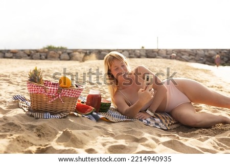 Cheerful young woman enjoy at tropical sand beach. Young woman taking a picture of fruit on the beach