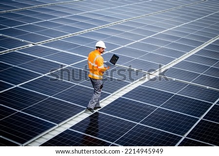 Renewable energy engineer walking through large solar power plant and checking electricity production on his laptop computer. Sustainable energy source and eco friendly technologies. Royalty-Free Stock Photo #2214945949