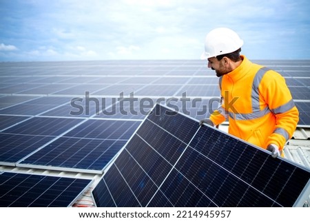 Industrial worker installing solar panels on the factory roof for inexpensive sustainable energy or electricity. Royalty-Free Stock Photo #2214945957