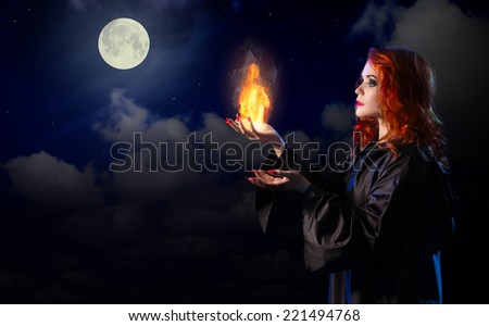 Young witch with flame on night sky background