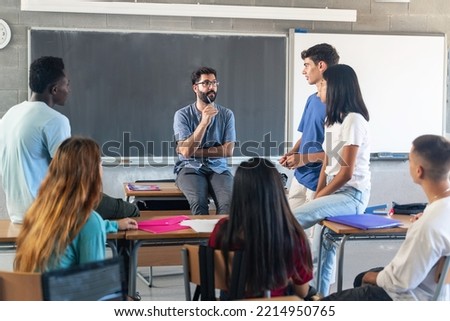 Group of teenagers with young male teacher at classroom, sitting talking and discussing together Royalty-Free Stock Photo #2214950765