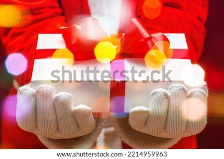 Santa Claus giving christmas present with gloved hands holding white giftbox tied up with red bow.Sparkling bubbles all around.Indoors shot,selective focus.