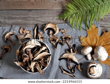 Dried and fresh champignon mushrooms in a bowl and on a cutting kitchen board. The idea of natural organic ecological products and their preparation for future use for autumn and winter. Royalty-Free Stock Photo #2214966555