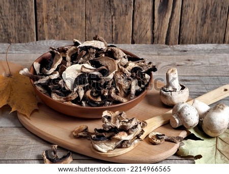 Dried champignon mushrooms in a bowl and on a cutting board. The idea of natural organic ecological products and their preparation for future use for autumn and winter.Autumn wooden background.