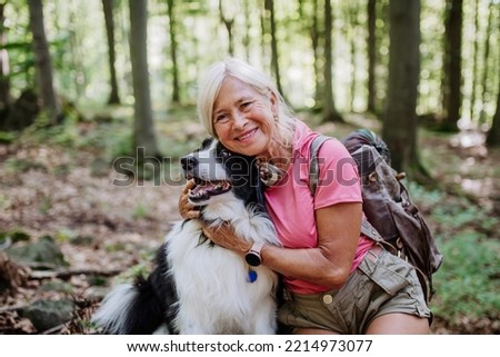 Senior woman resting and stroking her dog during walking in forest. Royalty-Free Stock Photo #2214973077