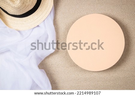 Empty beige round platform podium mockup for beauty cosmetics or products presentation. Straw hat and white crumpled linen fabric cloth on natural white beach sand background. Top view.