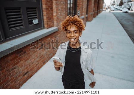 Young positive multiracial man in stylish clothes holding smart mobile phone. Looking at camera