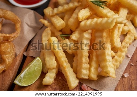 Homemade baked potato fries with mayonnaise, Tomato sauce and rosemary on wooden board. fast food products : onion rings, french fries on cutting board, on black stone background, unhealthy food.