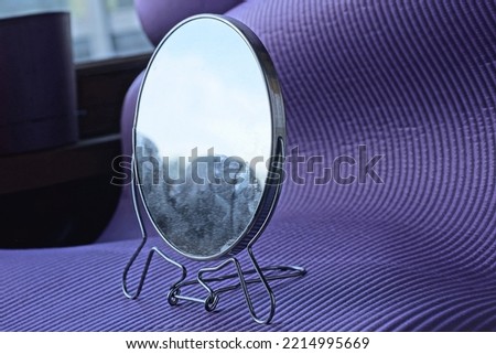 one small gray round mirror made of glass and metal stands on a lilac table in the room