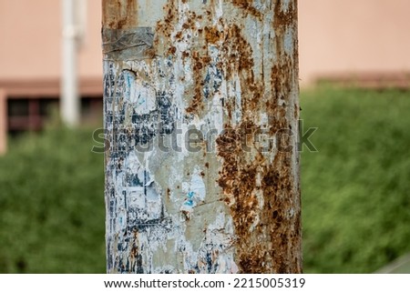 Old rusty pole with remnants of old posters with blurred grassy urban background. 