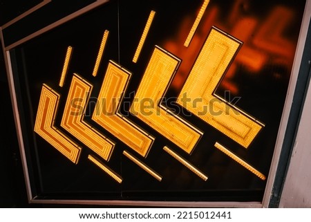 
Neon signs made of flashing arrows direct the way to an amusement park or arcade. Orange arrows in row against black background.