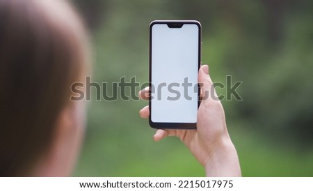 Female hand holding vertical black smartphone with green screen chroma key for tracking motion on the blurred city street background in sunny day. Close-up shot filmed in 1080p HD