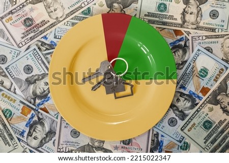 Credit and leasing. A plate with keys with a keychain in the form of a house on the background of scattered American dollar bills. Flat lay. Rental and purchase of real estate.
