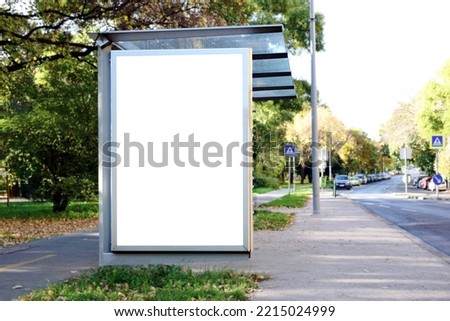 bus shelter with blank poster ad lightbox. bus transit stop. blank white billboard panel. glass structure. urban setting. city street. asphalt sidewalk. outdoor commercial space. background for mockup Royalty-Free Stock Photo #2215024999