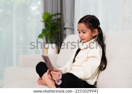 Asian little girl is using smartphone for internet and application in the living room. Concept of kid and technology, social media, entertainment, modern, lifestyle.
