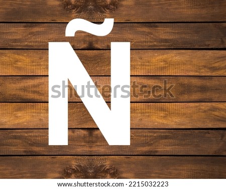 Ñ capital letter of alphabet in white hole on wood background