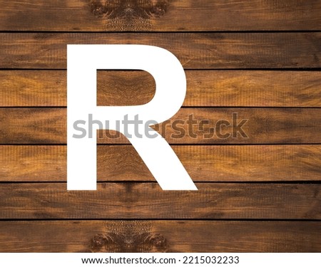 Alphabet letter R in white hole on wood background