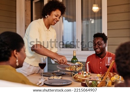 Portrait of smiling African American woman serving food to family while enjoying dinner together outdoors in evening