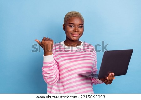 Photo of young girl smiling hold laptop directing finger empty space isolated on blue color background