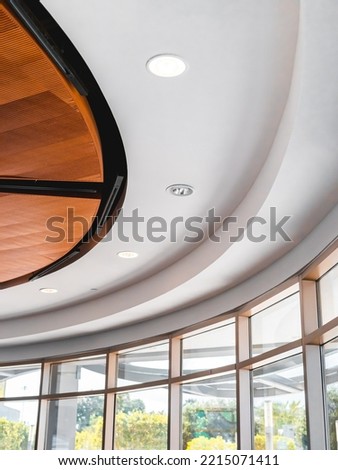 Curvy business interior roof with modern lights with arched style. Beautiful black, wood and white interiors from a coffee shop. Peaceful place to work and study. Elegance whites interiors and window