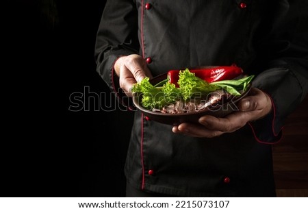 Professional chef presents his dish on a plate of sliced baked steak and vegetables. Space for hotel menu or recipe on black background