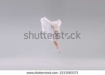 Portrait of young ballerina dancing, performing with transparent with fabric isolated over grey studio background. Weightlessness. Concept of classic ballet, inspiration, beauty, dance, creativity