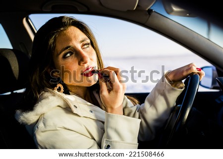 Beautiful woman applying lipstick while driving.