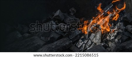 Red hot charcoal and a flame of fire. The texture of flaming burning firewood. Wide banner, flame background, close-up. space for text.