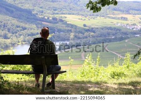 silhouette of a man sitting on a bench and resting while enjoying the view of the river down below Royalty-Free Stock Photo #2215094065