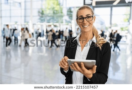 happy businesswoman with glasses at a trade fair holding tablet Royalty-Free Stock Photo #2215107457