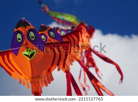 Funny Dragon Kite As A Long Garland With Orange Birds In The Blue Sky.