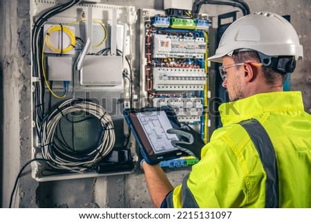 Man, an electrical technician working in a switchboard with fuses, uses a tablet. Royalty-Free Stock Photo #2215131097