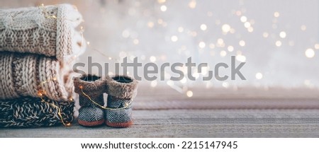 Stack of cozy winter knitted sweaters and cute small boots on a blurred background with bokeh. Warm Cozy Concept. Banner imafe for design. Royalty-Free Stock Photo #2215147945