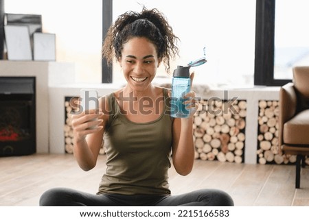 Online vlogging blogging training on fitness mat using cellphone. African young female athlete doing yoga exercises at home, having videocall, video tutorial, taking selfie Royalty-Free Stock Photo #2215166583