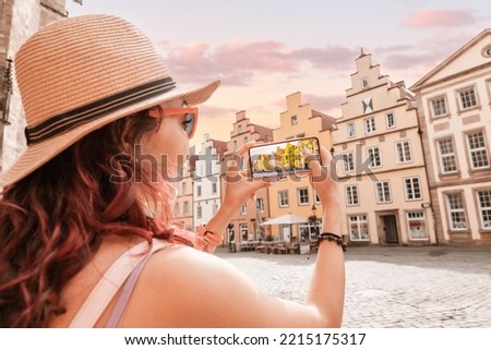 Travel blogger takes photos on the camera of smartphone of the Osnabruck historical houses building in old town market square, Germany